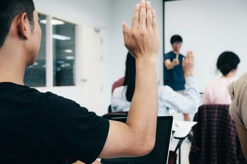 A student with his hand up asking a question. Possibly about Do I have to pay for WordPress if I have Bluehost.