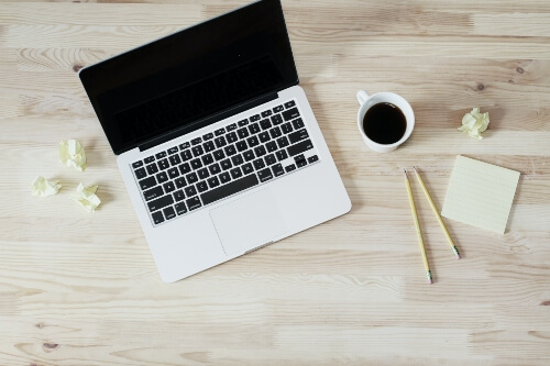 A top view of a blogger's laptop, sticky pad, pens and a cup of black coffee.